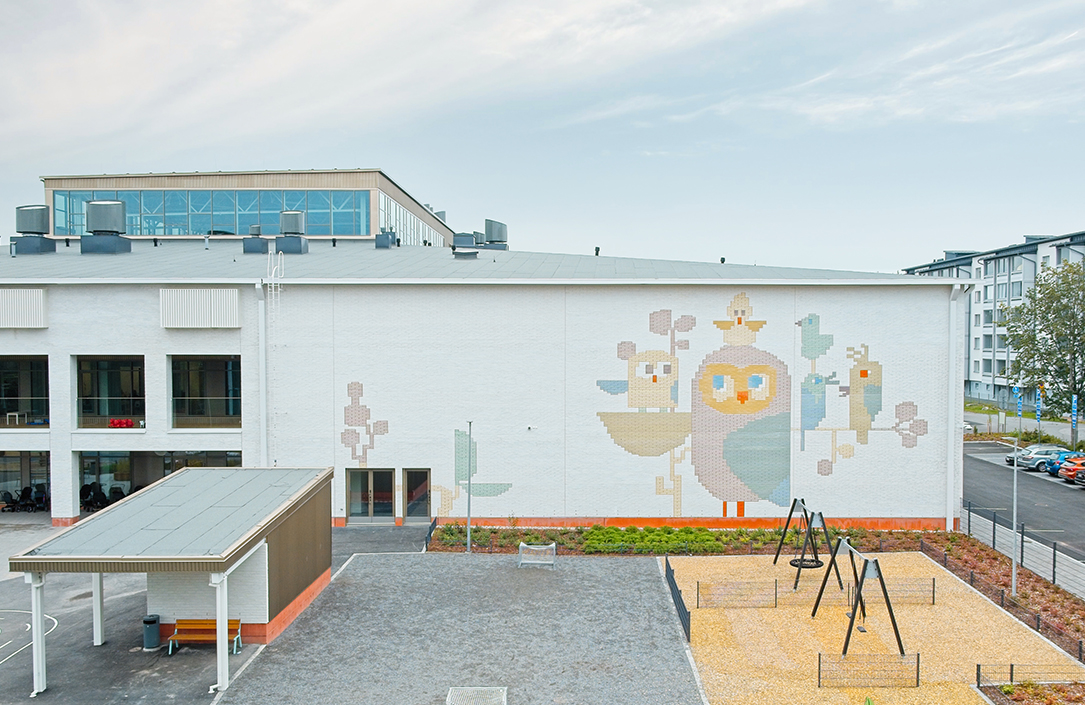 Koulurakennuksen yhtenäinen ulkoseinä, jossa linnun kuva toteutettu tiililadonnalla.
