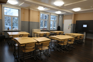 Luokkahuone, jossa pulpetteja, puolipaneelit ja keltainen tapetti.