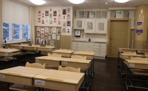 Puurakennuksen luokkahuone, jossa edessä pulpetteja, takaseinällä oppilaiden piirrustuksia.