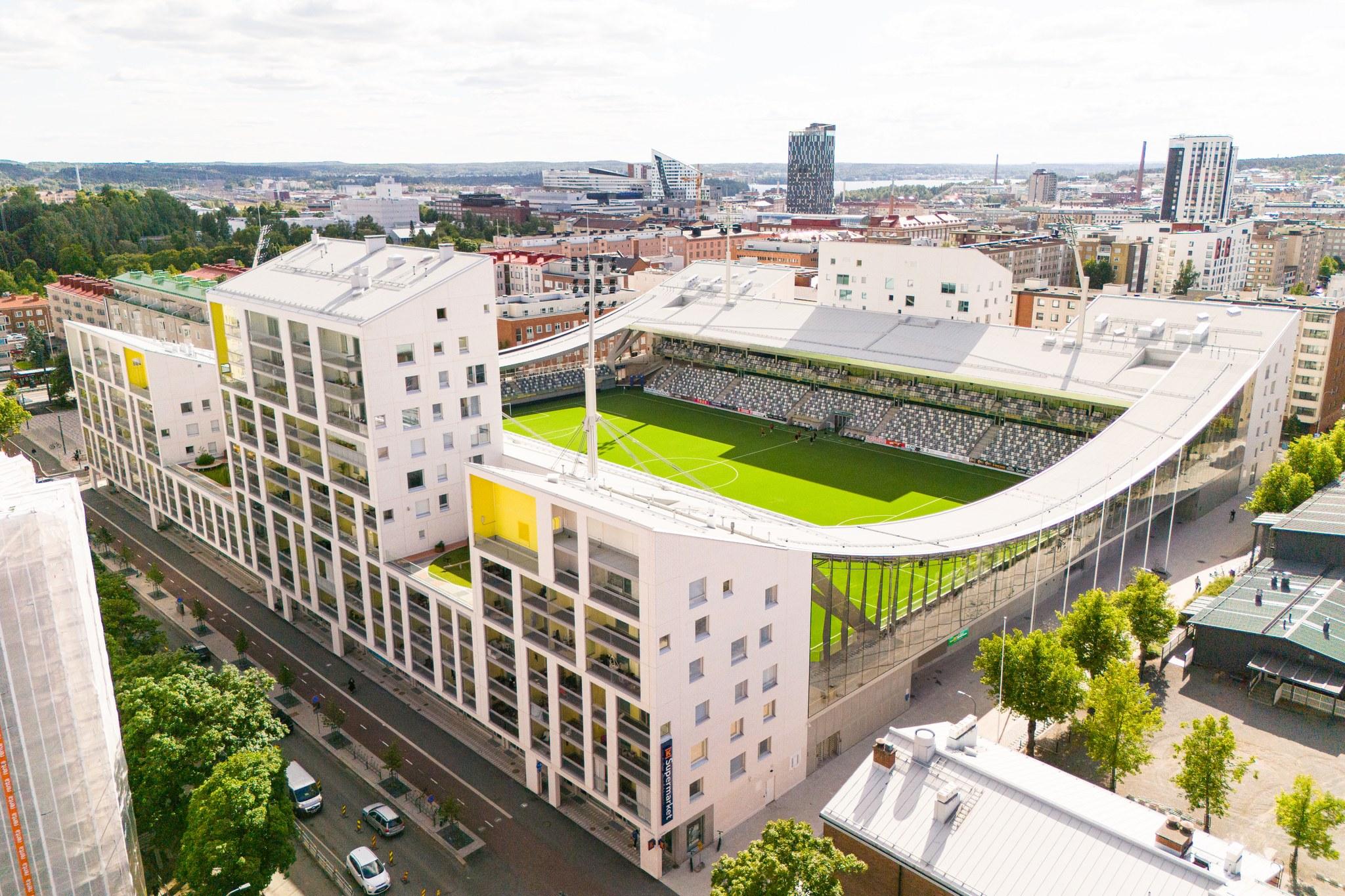 Suuri jalkapallostadion, jossa kaarevat päädyt ja etualalla stadionin yhteydessä oleva kerrostalo.