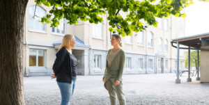 Kaksi naista seisoo koulun pihalla ja keskustelee.