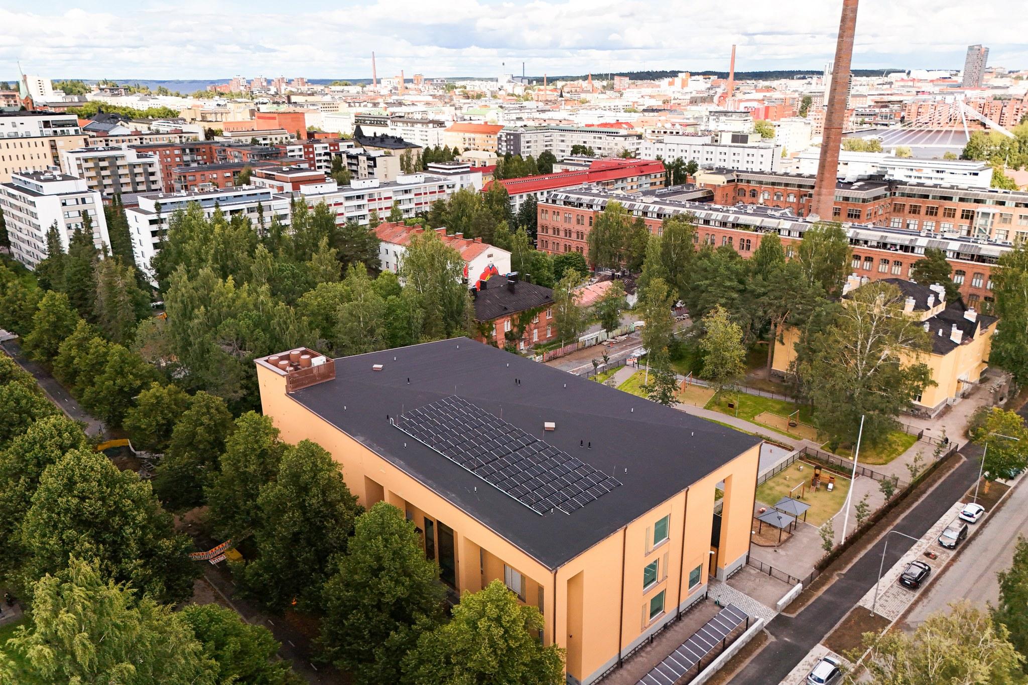 Koulurakennus ilmasta käsin kuvattuna; näkyy koulun katto sekä taustalla paljon kaupungin rakennuksia.